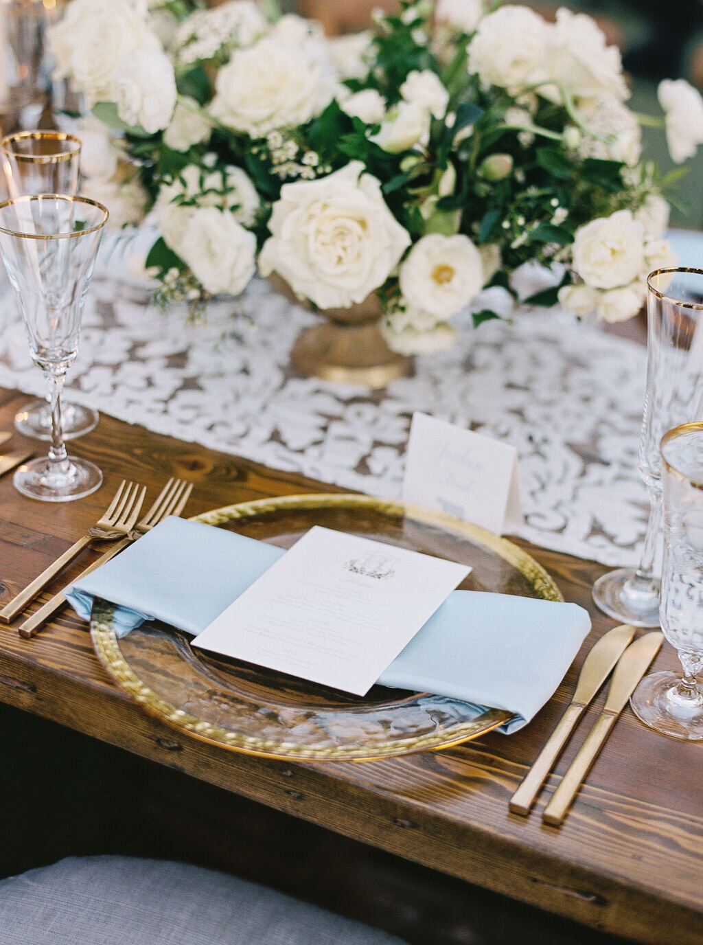An elegant wedding reception table with gold accents, crystal glassware, and lush white florals. The perfect inspiration for a sophisticated and timeless wedding.