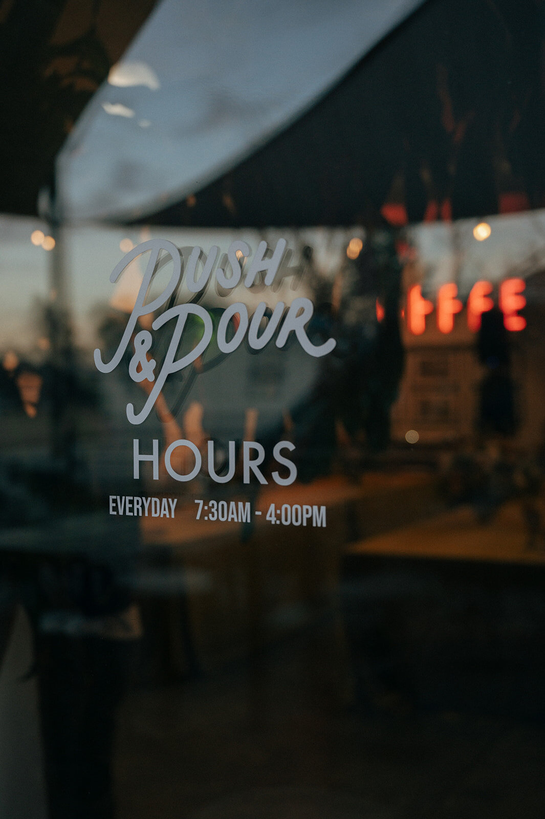 The reflection of a door window that has the words push and pour hours.