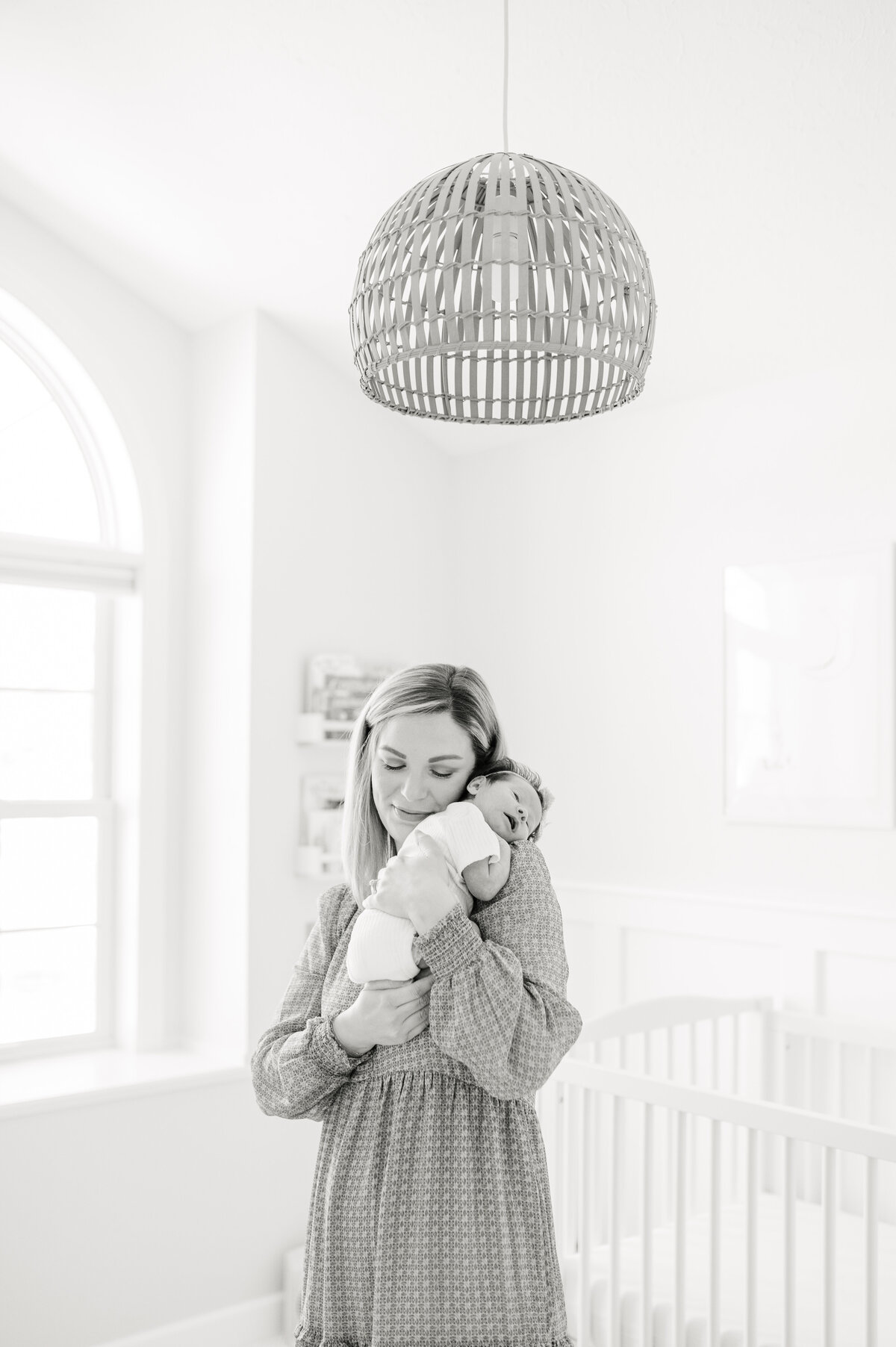 Black and white image of mom holding her baby on her shoulder in their nursery