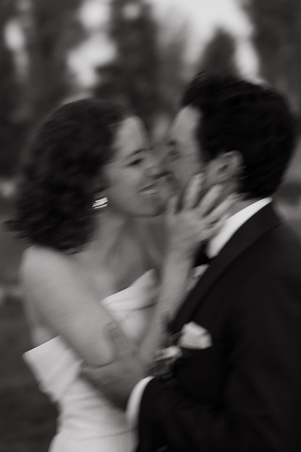 Black and white photo of a bride and groom smiling and holding each other's face, the photo is blurry with movement