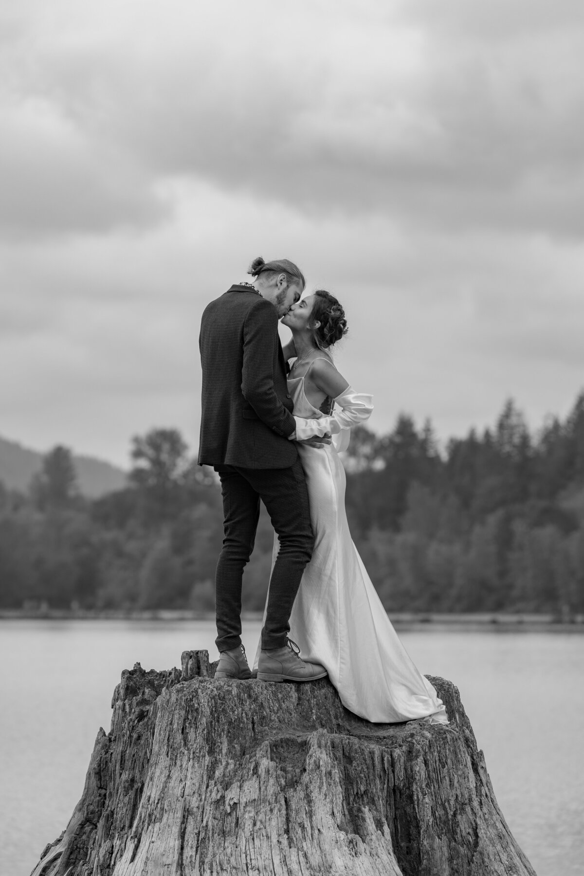 A newlywed couple kissing while on a tree stump