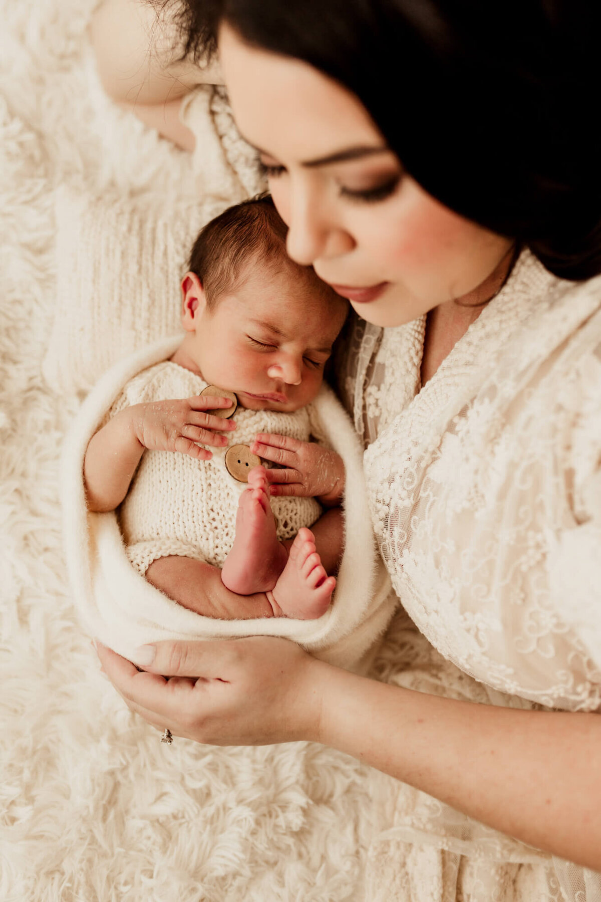 Mother lays next to her baby boy as he sleeps in a white custom knit romper.