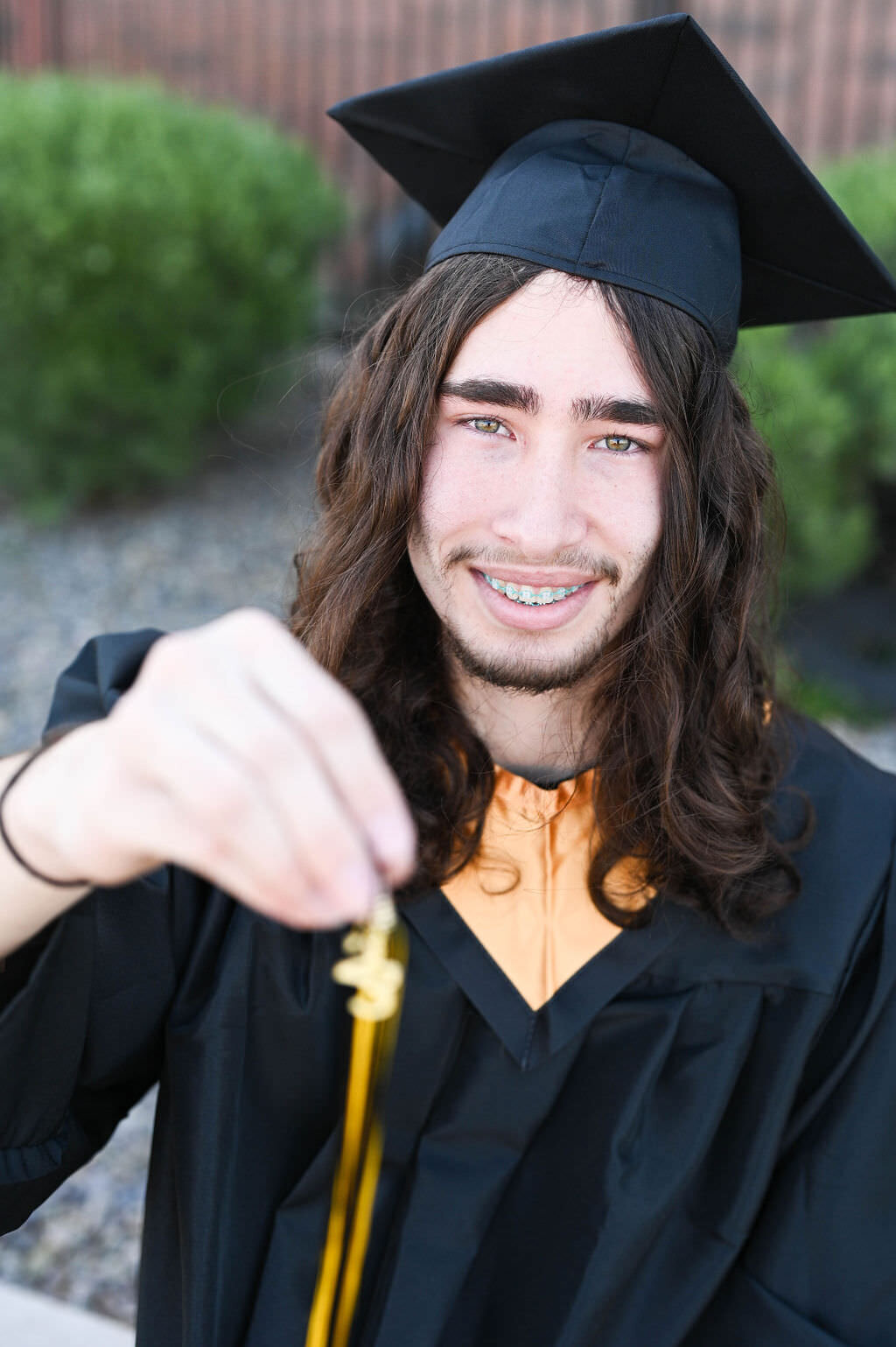A man smiling and holding up a graduation tassel.
