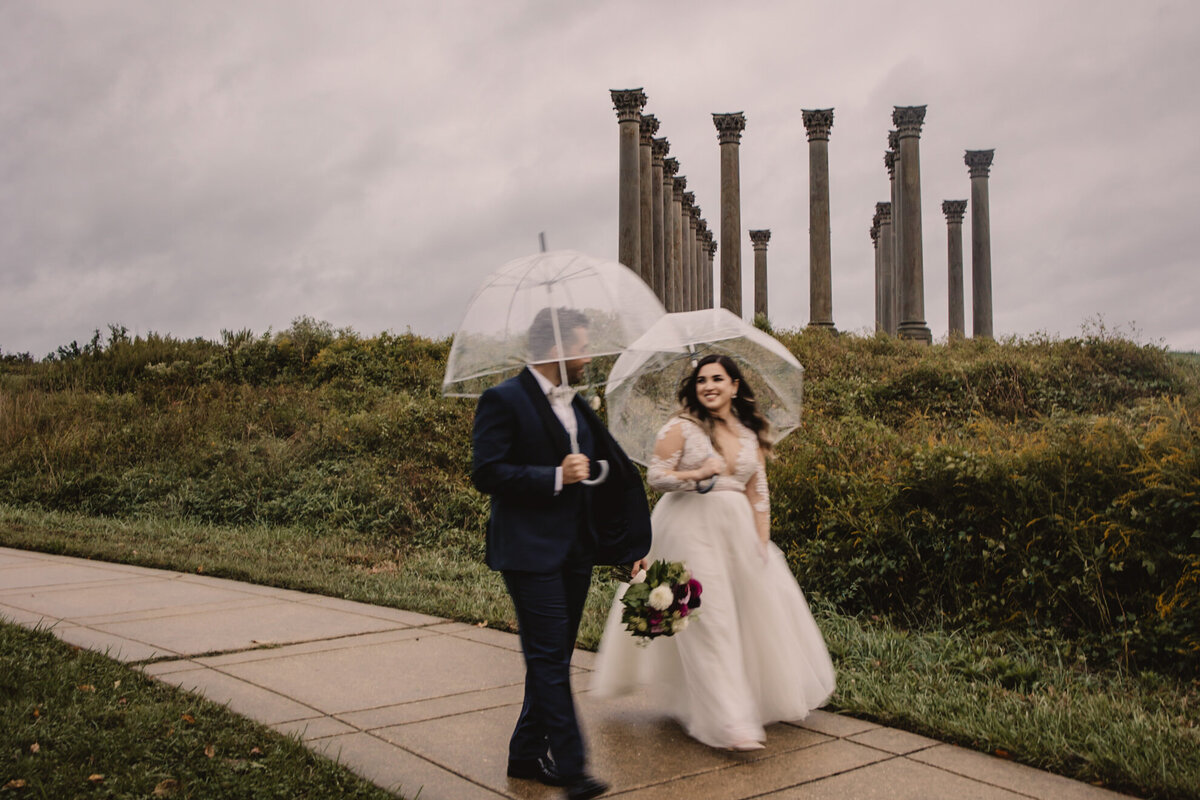 A wedding couple holding umbrellas and walking on a sidewalk 
