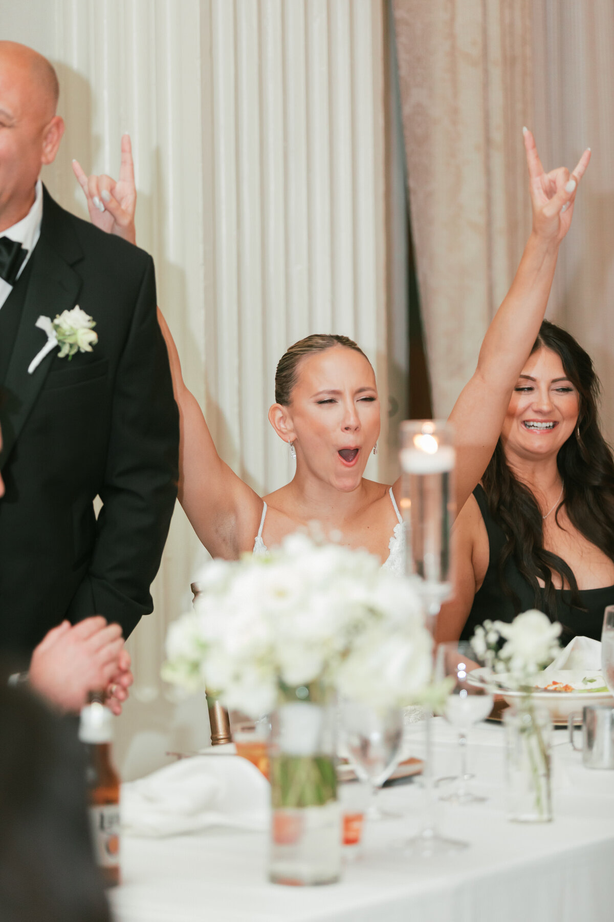 Bride cheers at reception table, full of excitement, captured by Philadelphia wedding photographer.