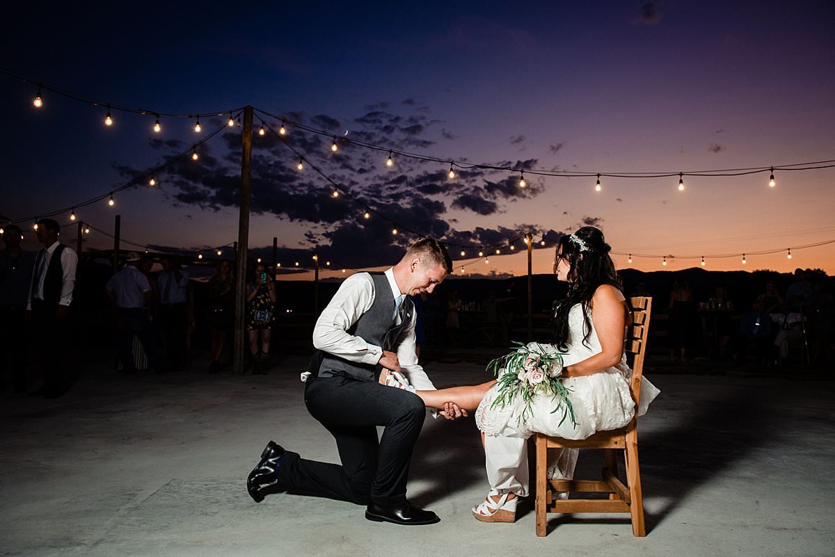 Groom removing garter on the outdoor patio at Headwaters Ranch during a orange and purple Montana sunset
