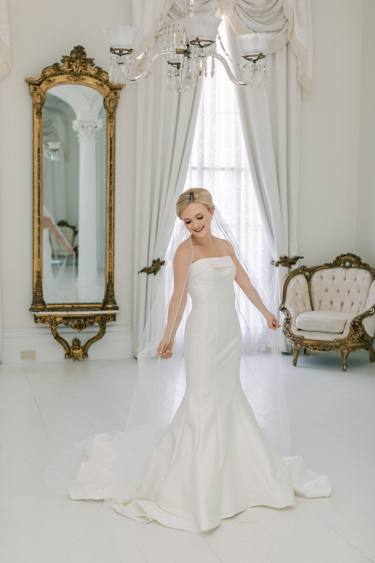 A bride holds the veil in a white room.