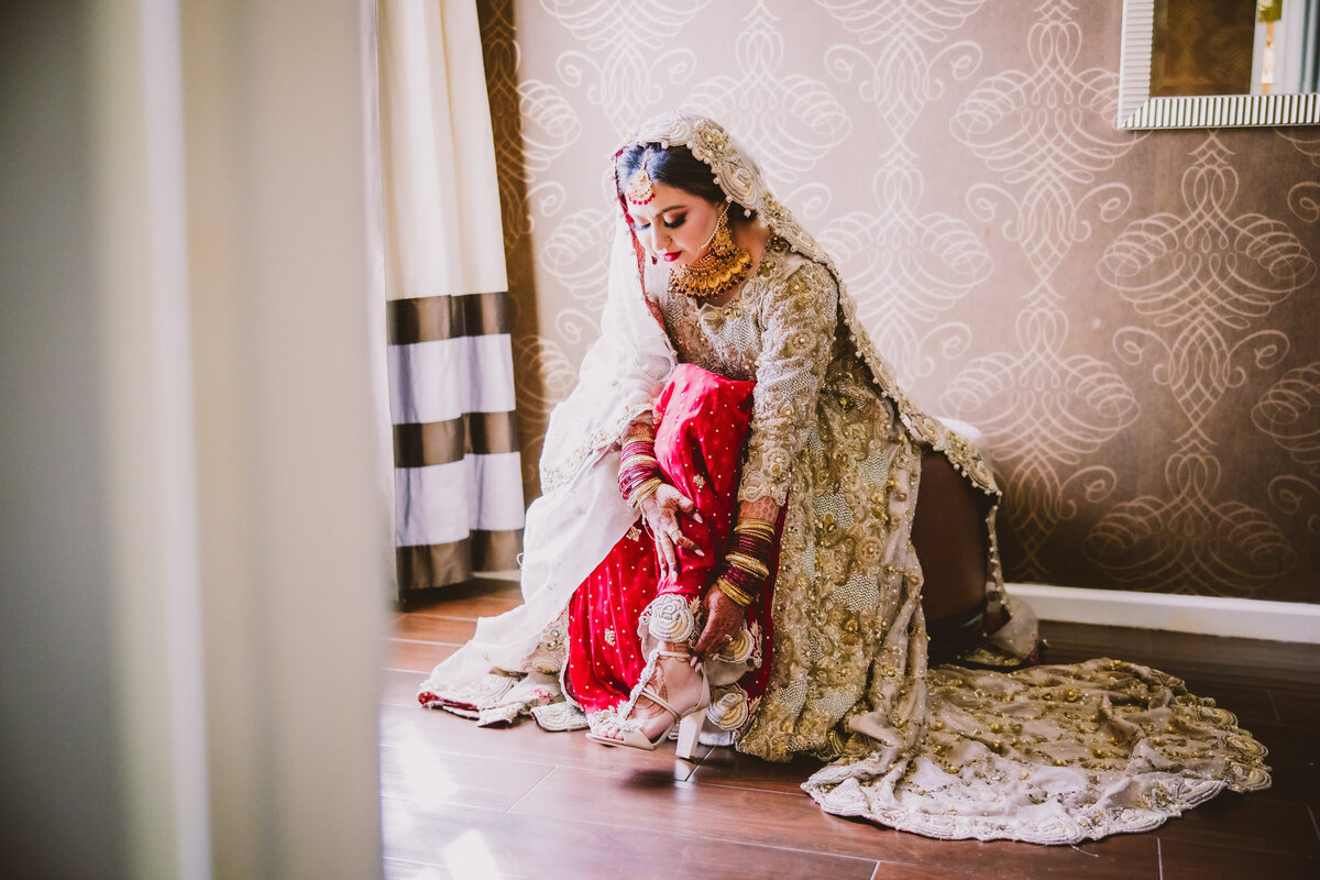 pakistani bride getting ready by putting her shoes on at the hotel in long island ny