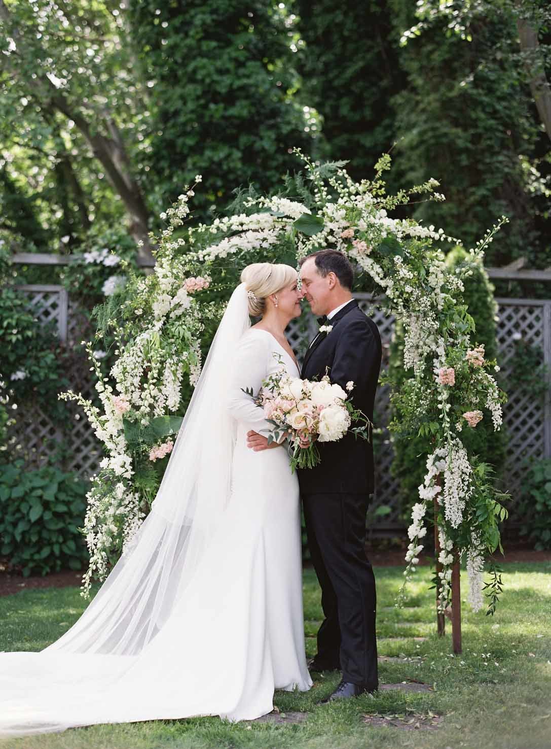 bride and groom in fron to white wedding arbor decorated with white delphinium