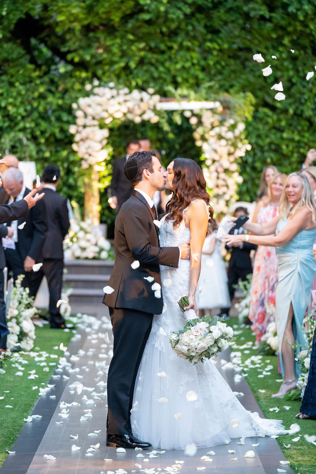 bride and groom kissing while guests toss petals