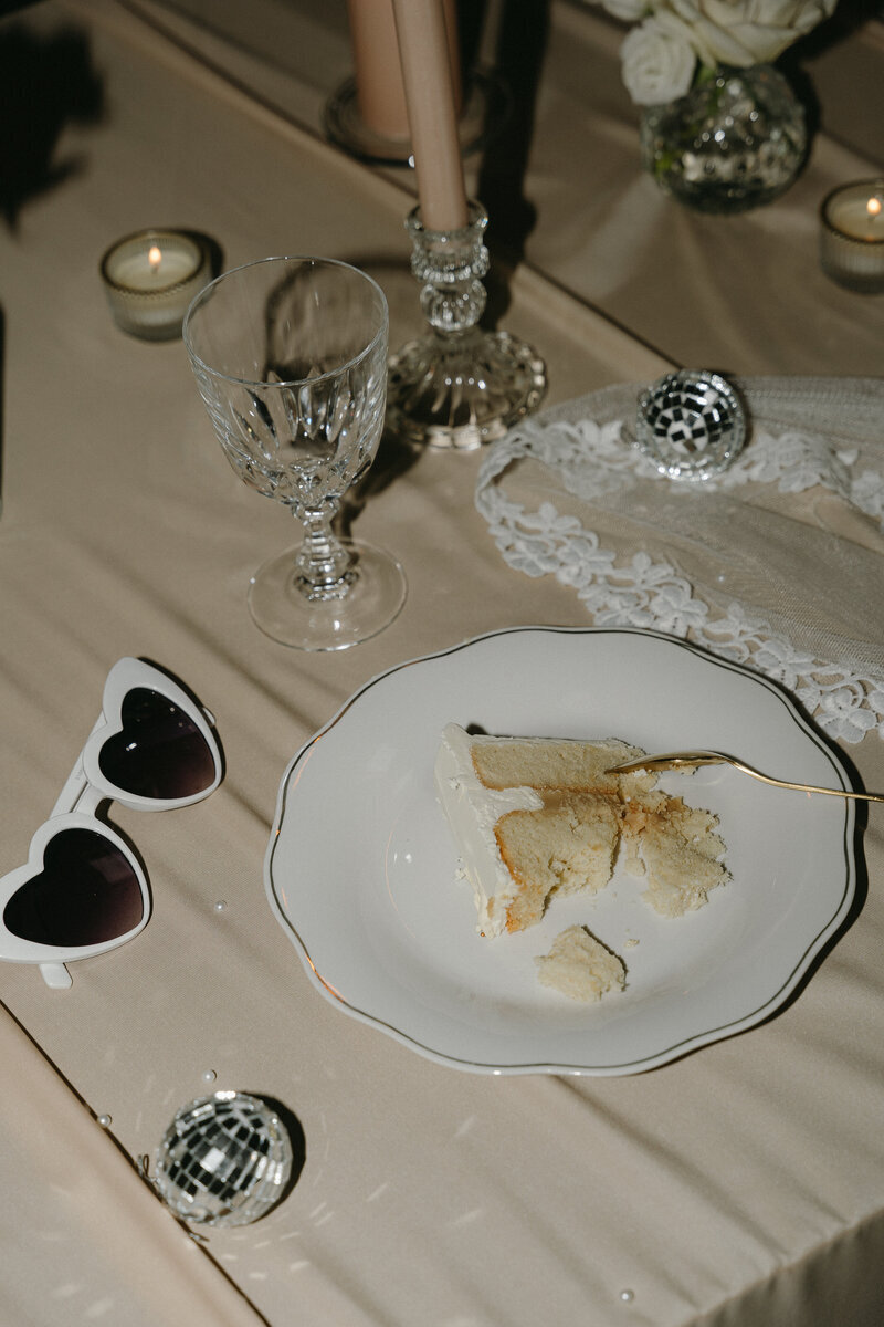 Assiette avec wedding cake sur table décorée de lunettes en formes de coeur, vaisselle et boules à facettes. Scénographie imaginée par Nos moments ensemble, décoratrice de mariage Loire Atlantique & Vendée.