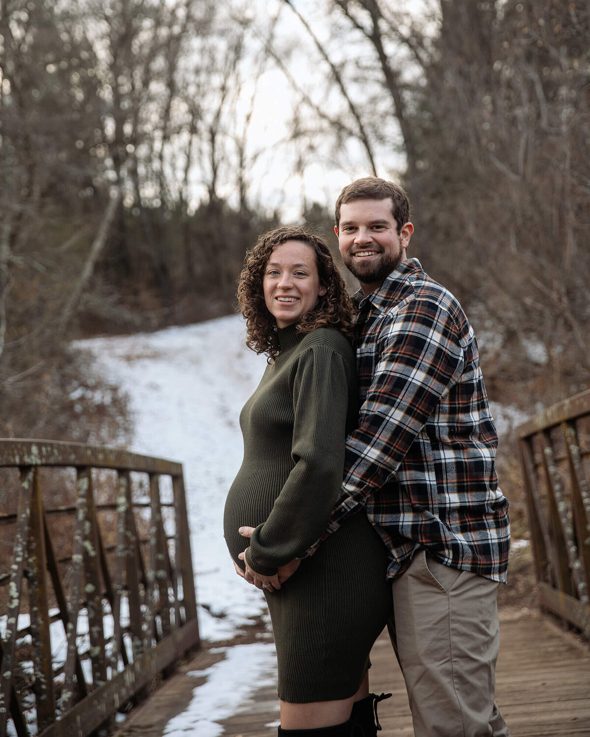 Husband wrapping his arms about pregnant wife on a winter day.