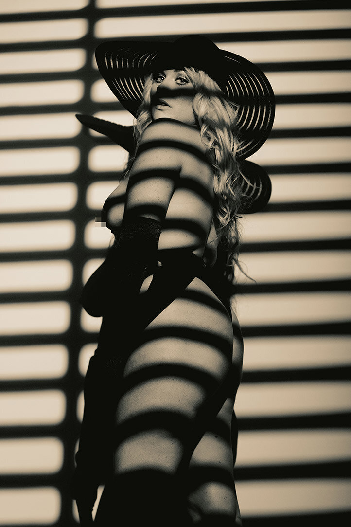 A sensual fine art nude image of a woman in gloves, boots, and a hat with black and white GOBO blinds lighting.