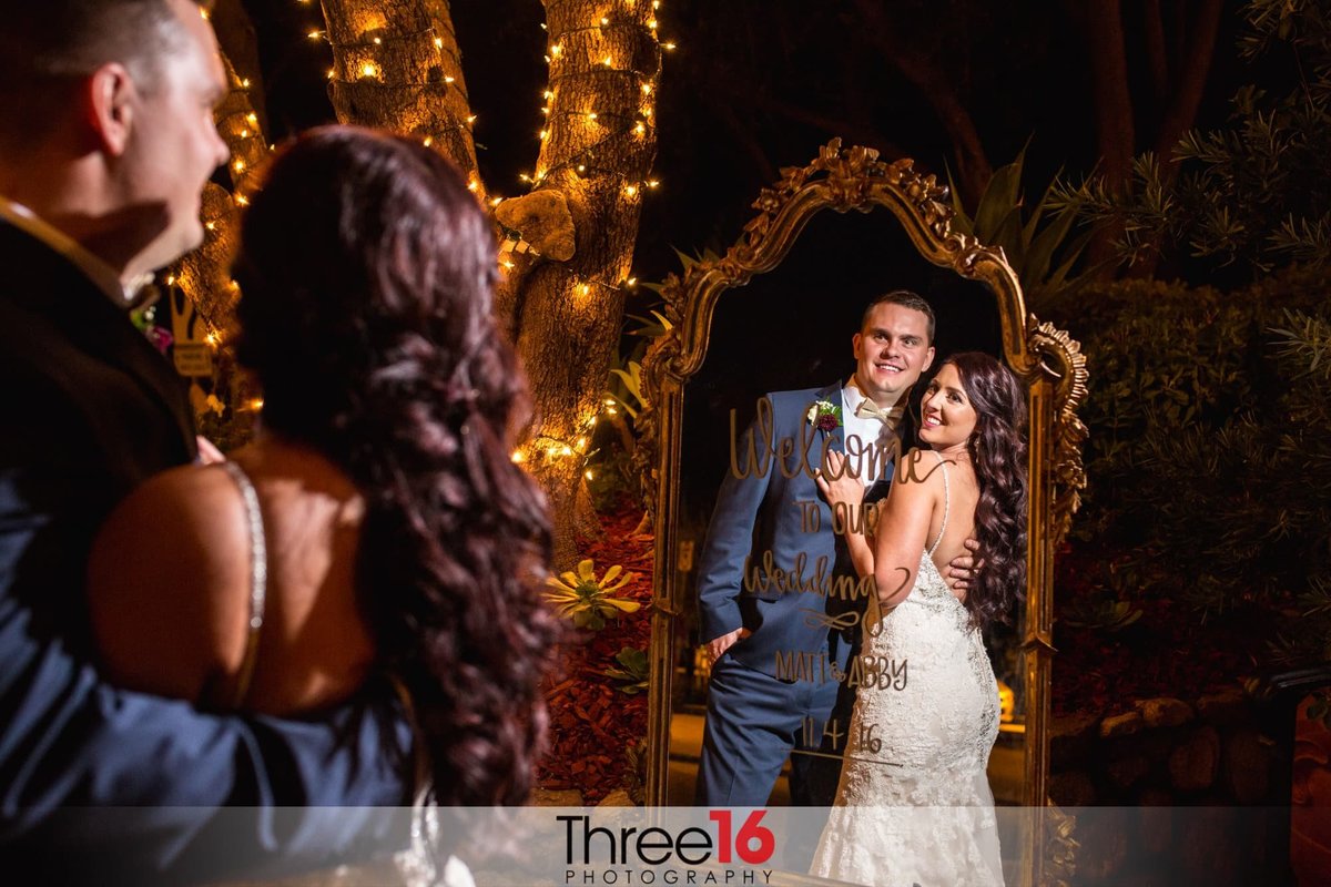 Bride and Groom pose in front of a mirror that welcomes their guests