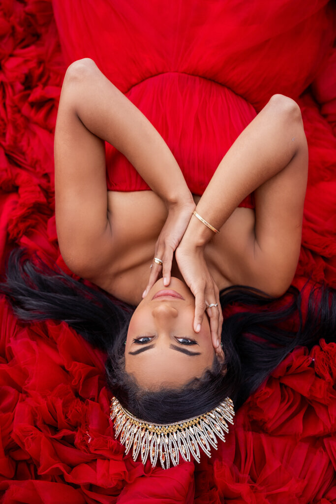 Intimate portrait photography of young woman with crown laying on red fluffy dress