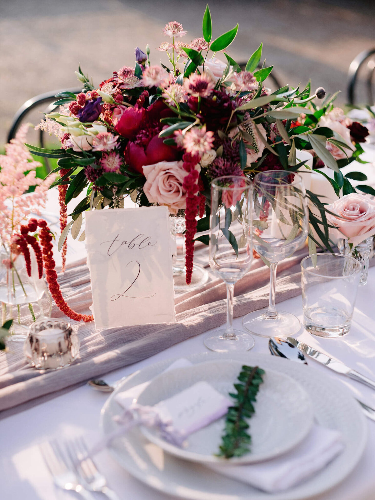 The flower bouquet centerpiece, wine glasses and plates are on a white table, with a sign that reads, "table 2".