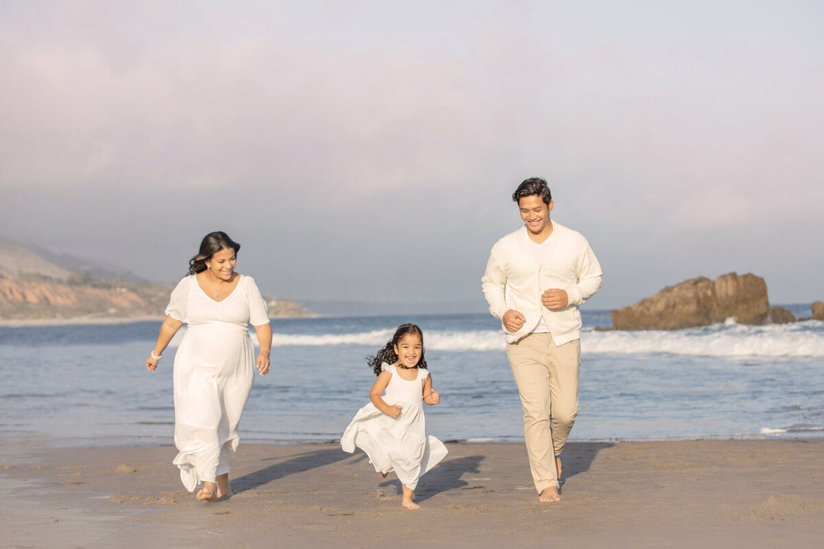 Mom, dad and little girl playing at beach in Malibu all wearing white