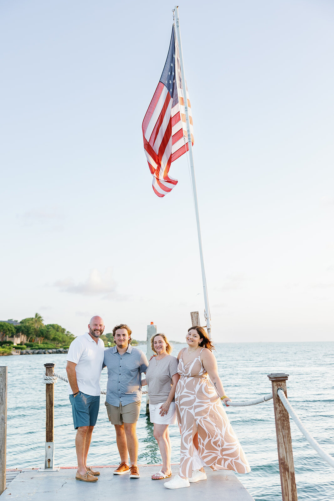 A family stands proudly by an American flag on the dock, overlooking the ocean, during a Florida Keys portrait session.