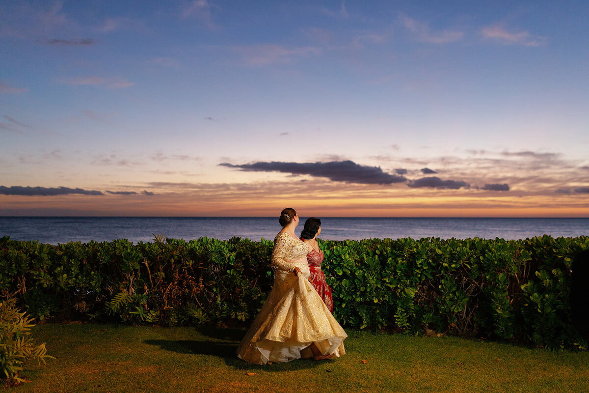 A newlywed couple holding hands and looking out over the water at sunset 