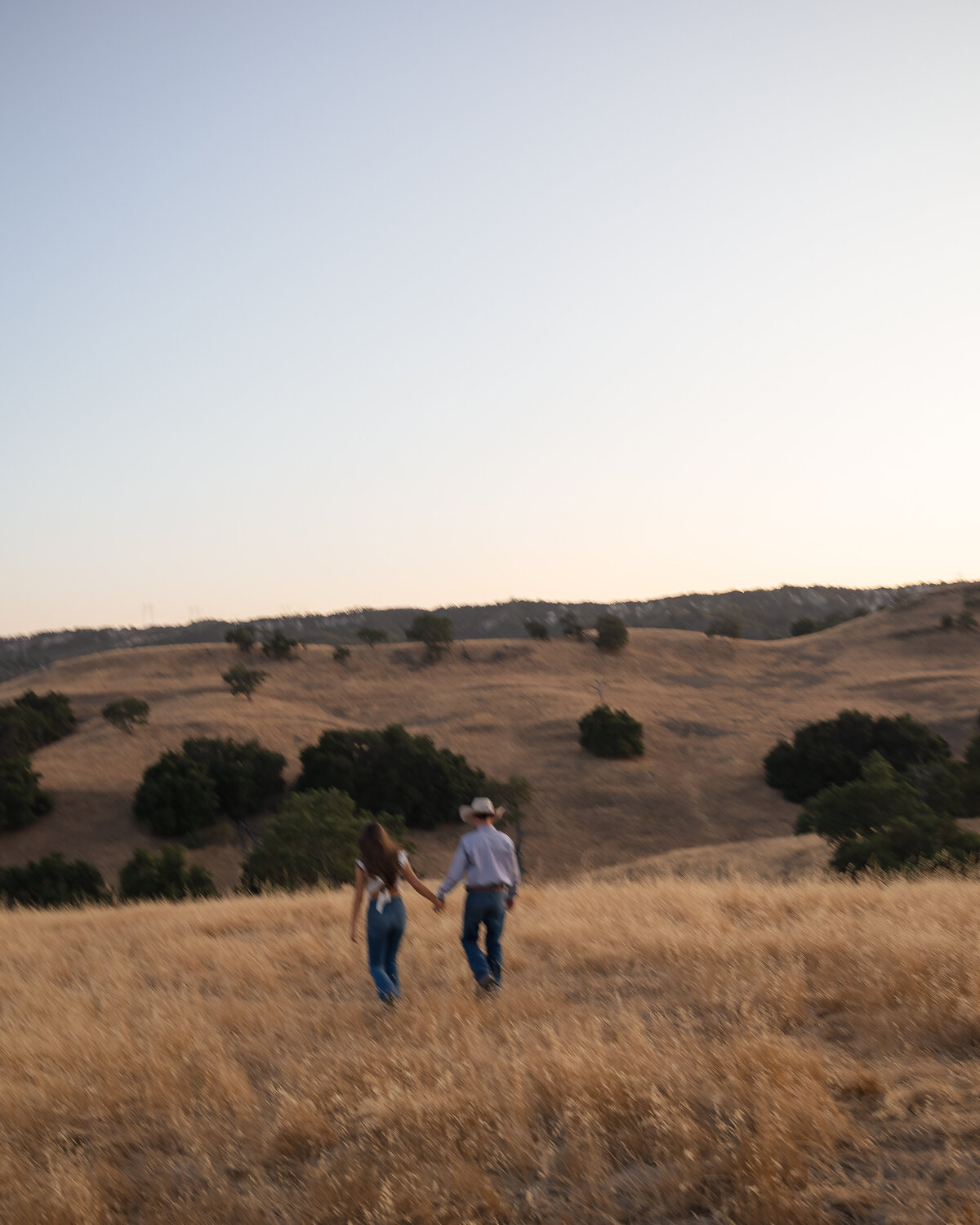 candid couples engagement photos in open field during golden hours running in San Luis Obispo