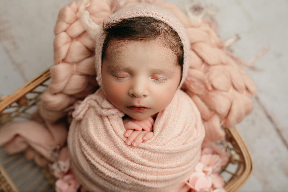 close up of newborn sleeping in a pink wrap in the basket