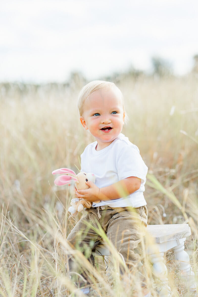 a toddler boy sits on a stool in a field of tall grass and is candidly captured by an Austin family photographer.