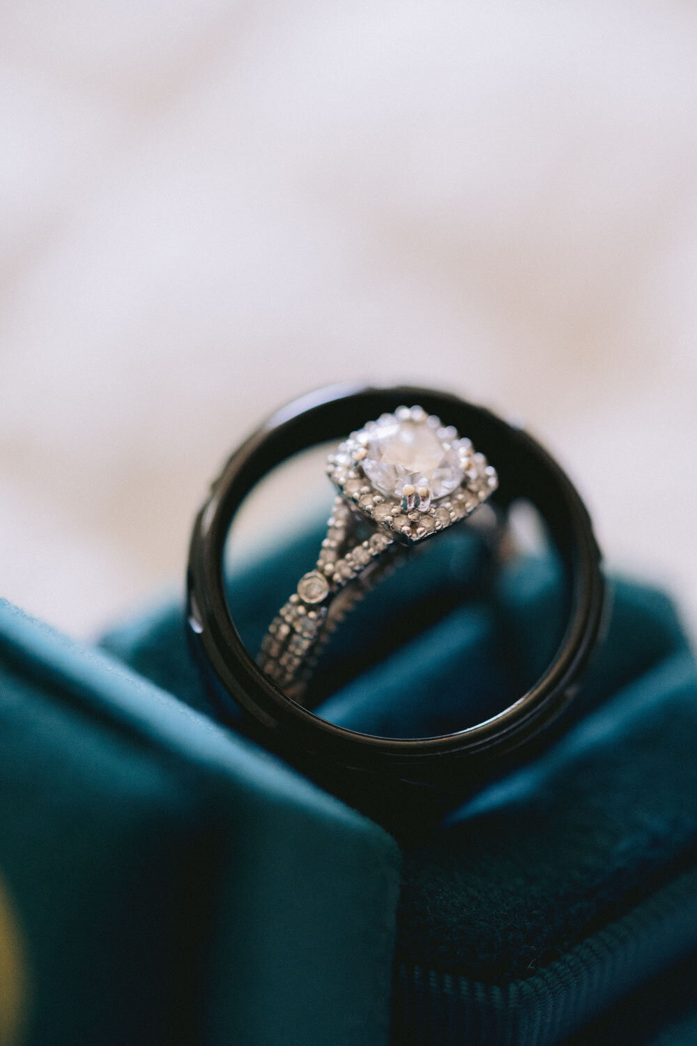 Engagement ring inside a black wedding band on a teal velvet box
