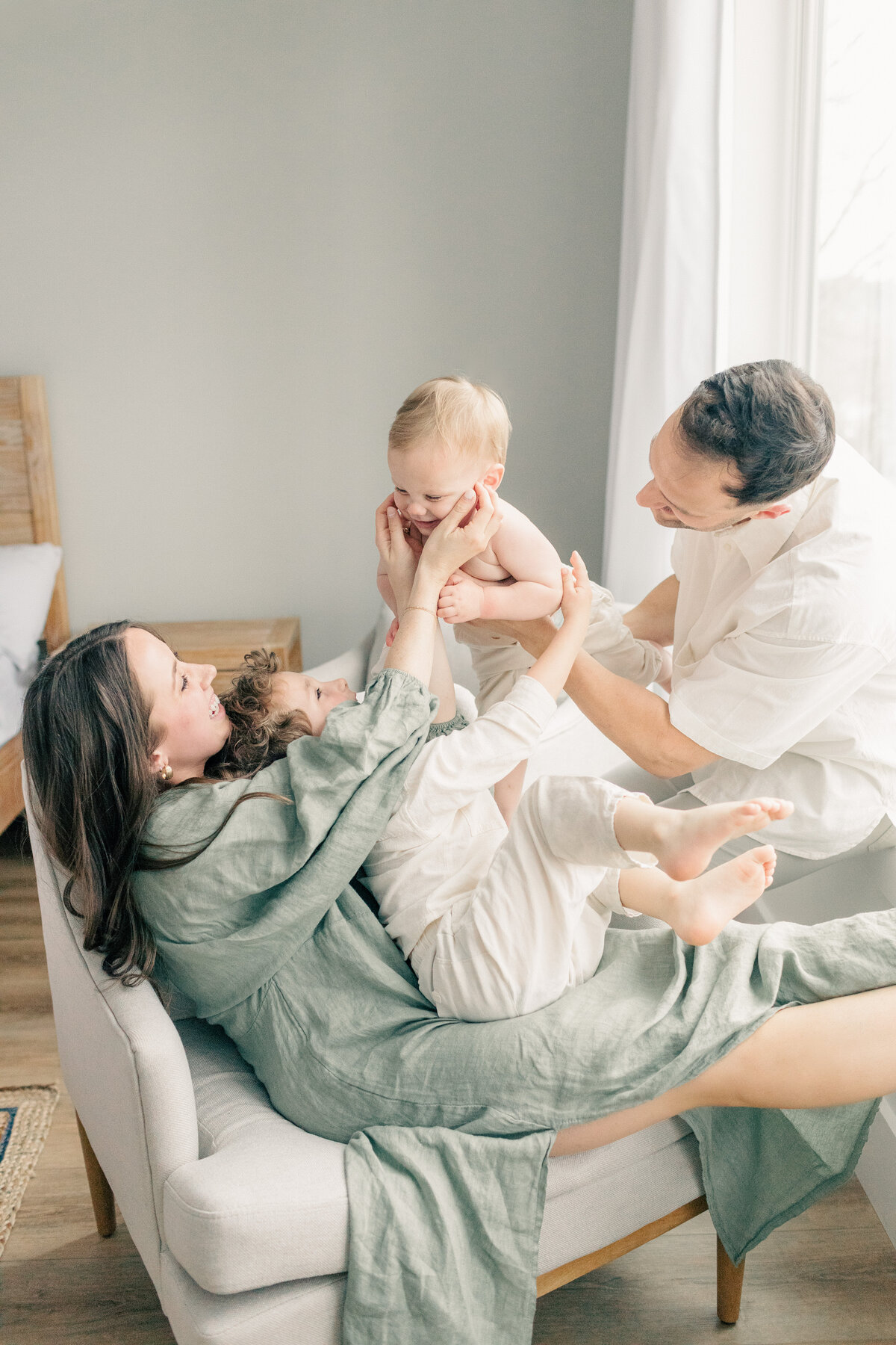 Family picture of mother, father, and two sons as they joyfully tickle each other during their in home session in Kansas City
