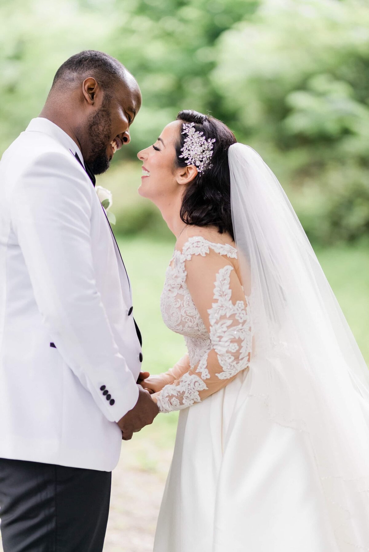 Bride and groom both wearing white, smiling at each other, holding hands, in multicultural wedding.