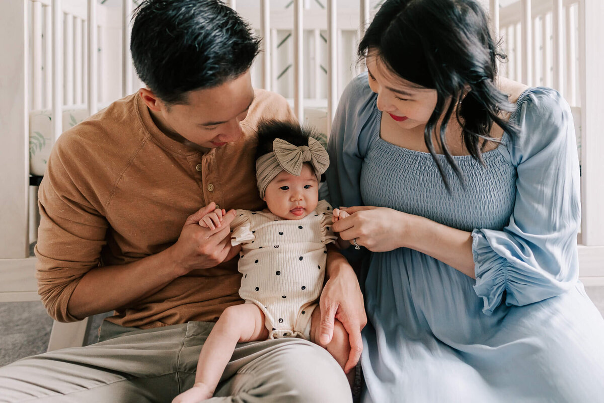 Parents sitting in front of the crib holding their newborn daughter