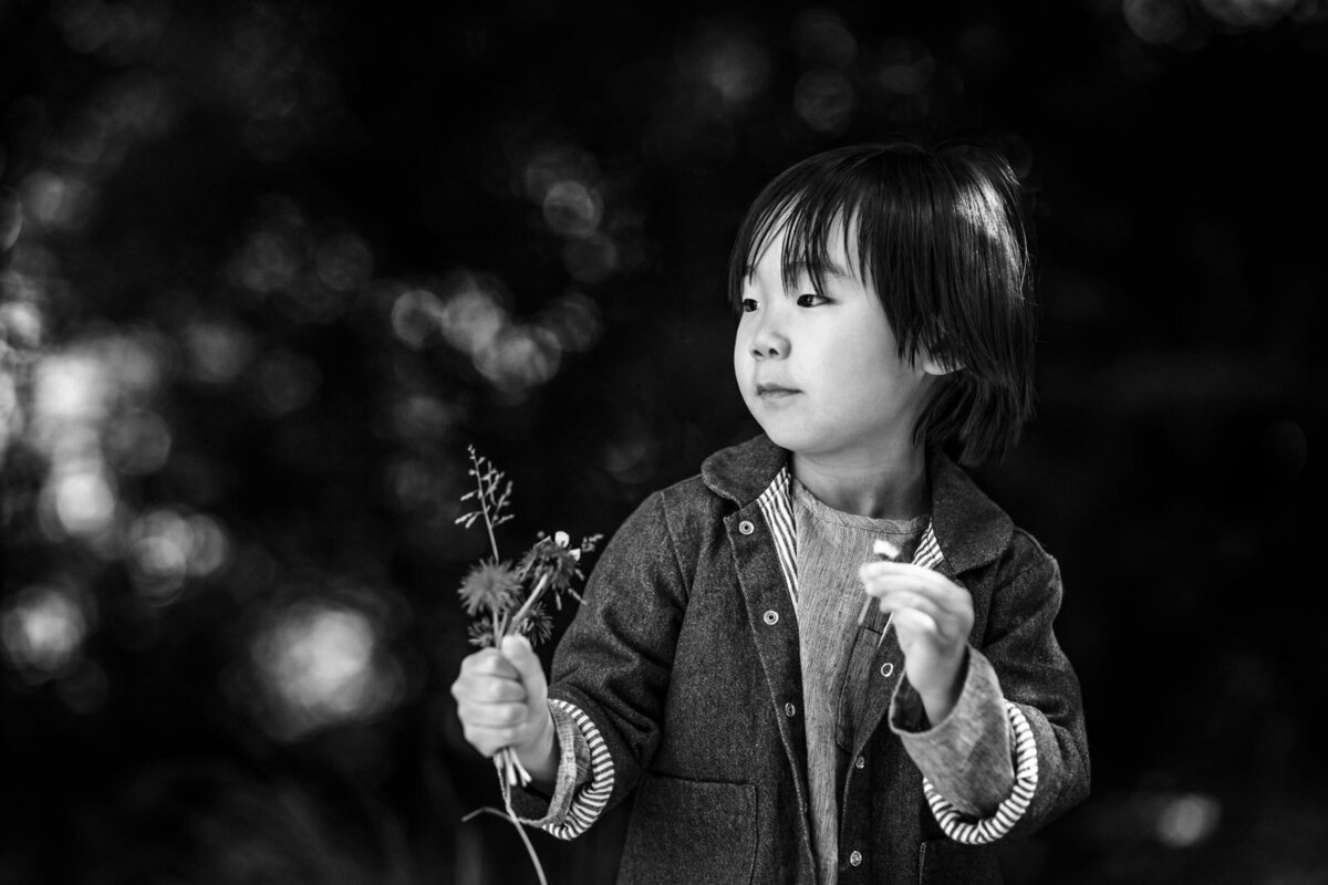 5-year-old boy standing in a park holding a plant and looking away from the camera