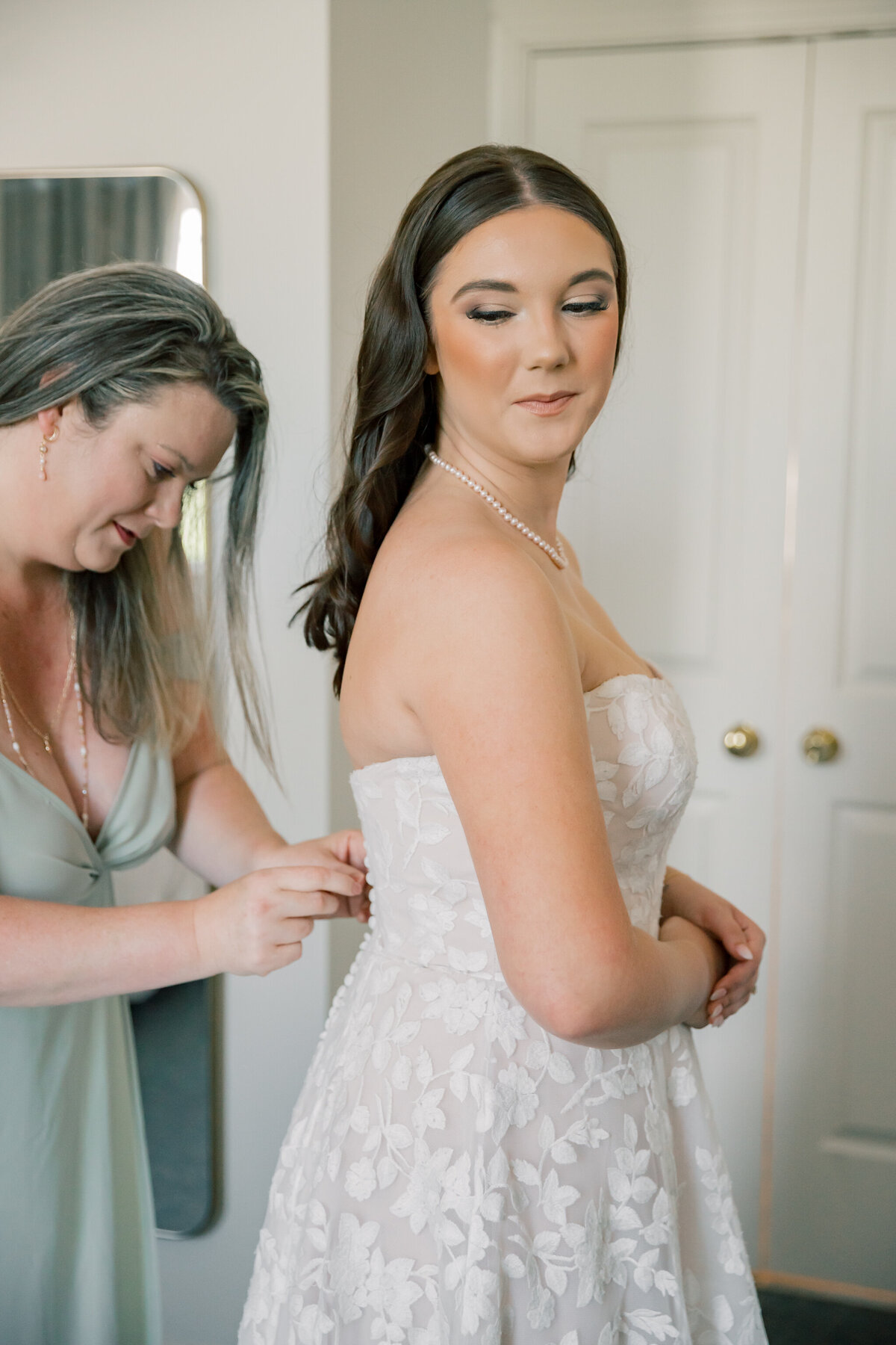 Bride's mom helps zip up her dress before wedding ceremony at Three Oaks Manor
