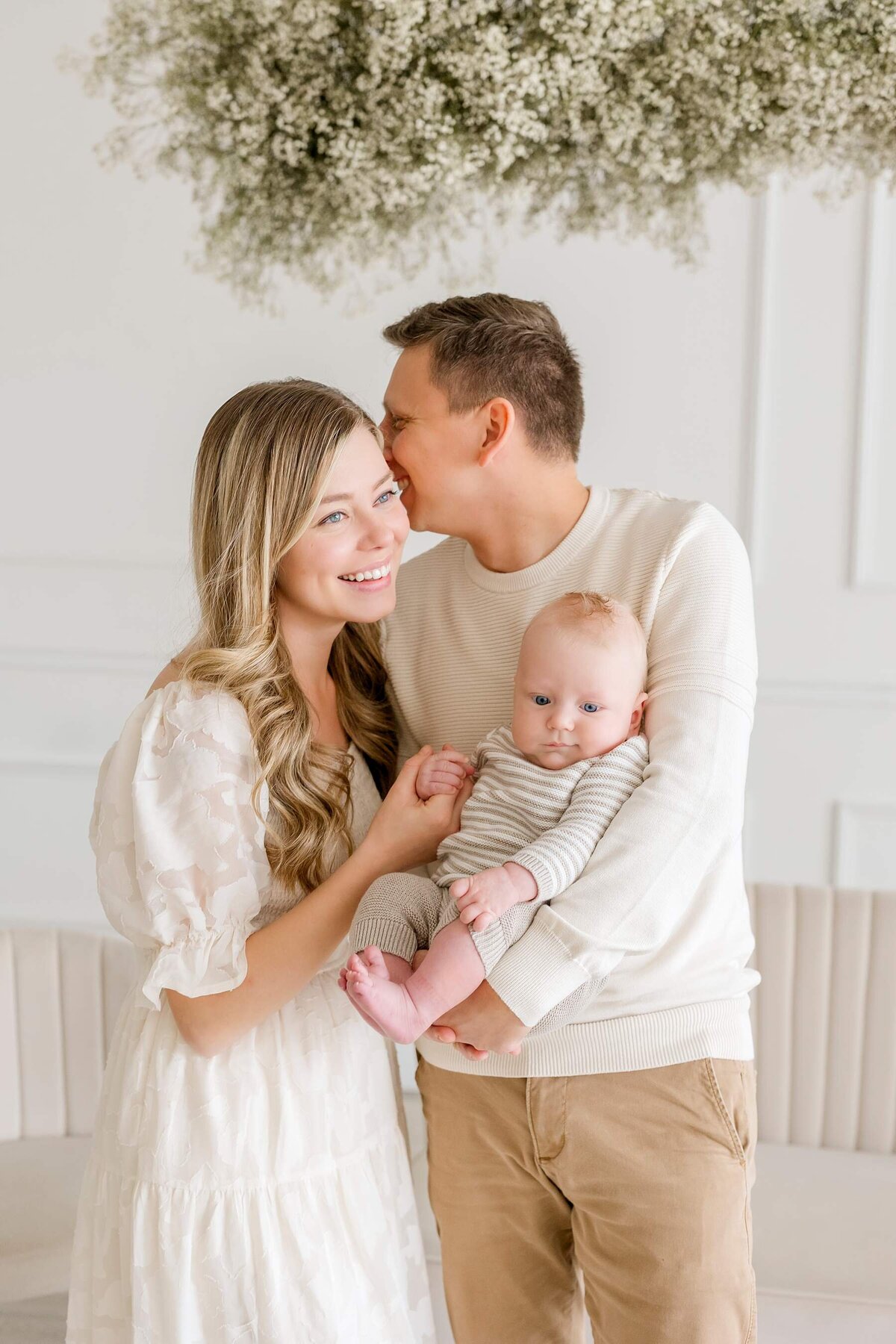 mom and dad cuddling for pictures with their newborn son