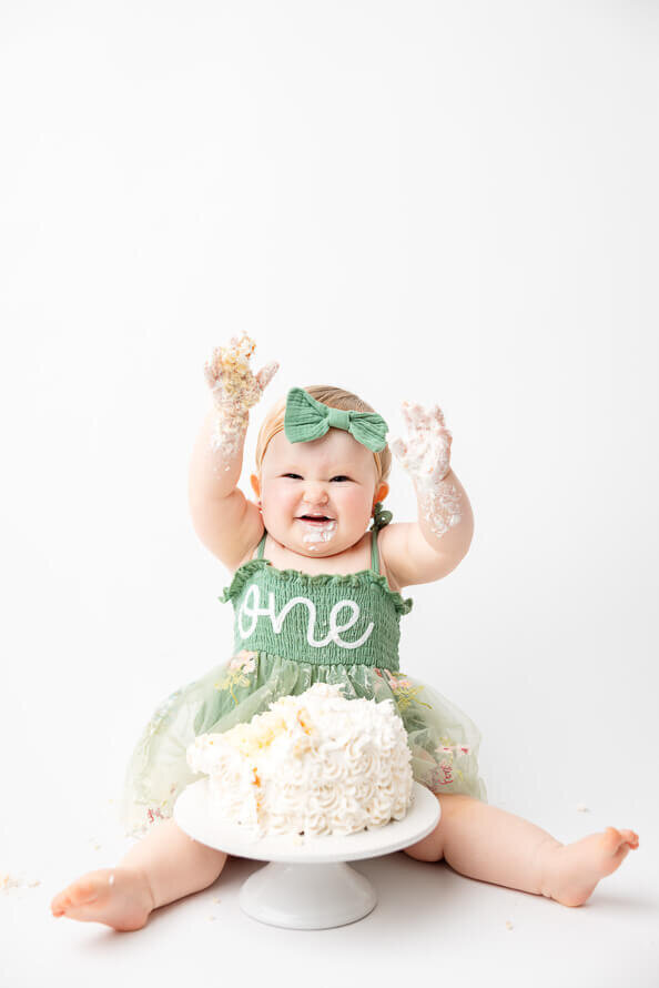 Baby girl holds cake-filled hands up for her photoshoot.