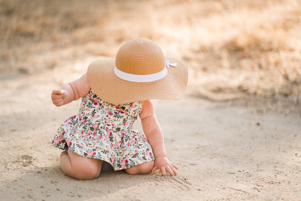 one year old girl wearing a hat and looking down at the ground