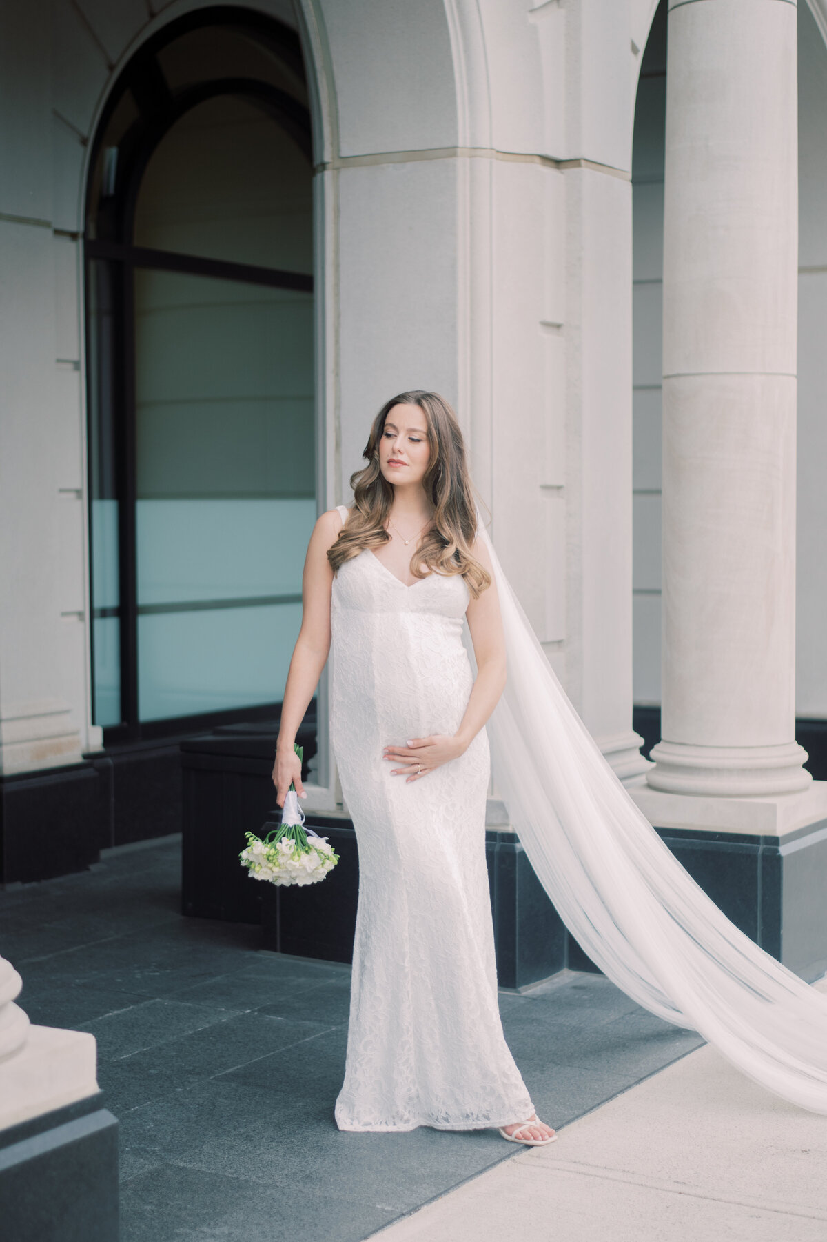 Bride posing on the wall holding baby stomach and holding flower in Oakville