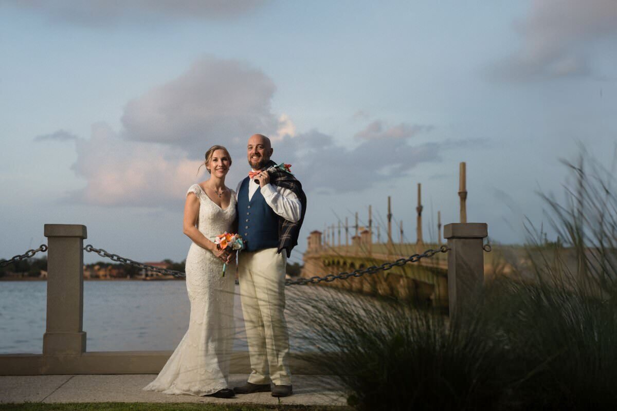 Newlywed couple in wedding attire posing at historic St. Augustine bayfront with Bridge of Lions in background during golden hour elopement photography session