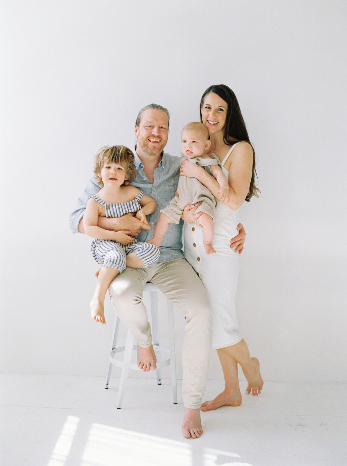 Seattle Family Photos  taken in all white studio, with one toddler and one baby, family in all white gray and blue outfits 