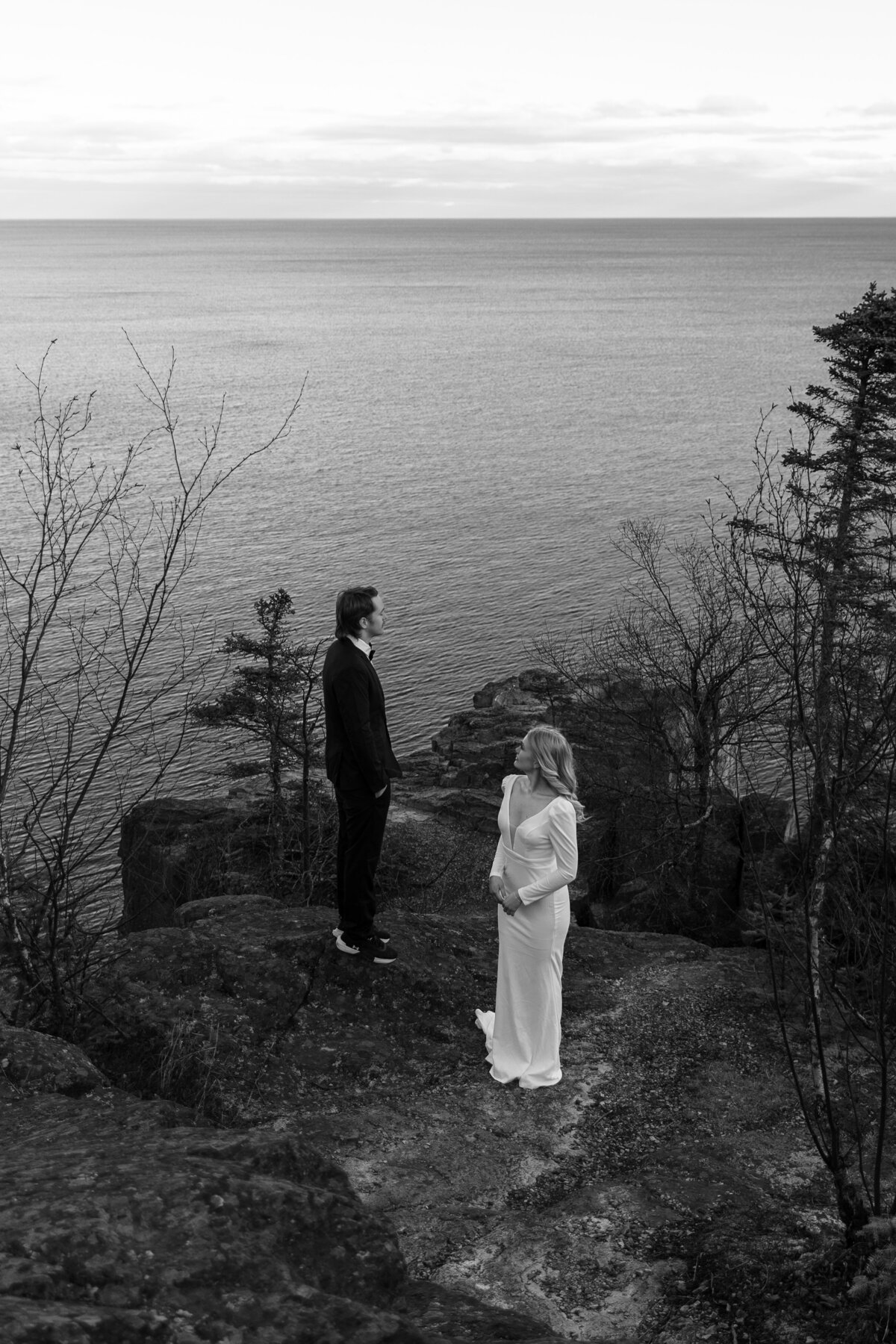Black and white photo of elopement couple looing over a cliffside at lake superior 