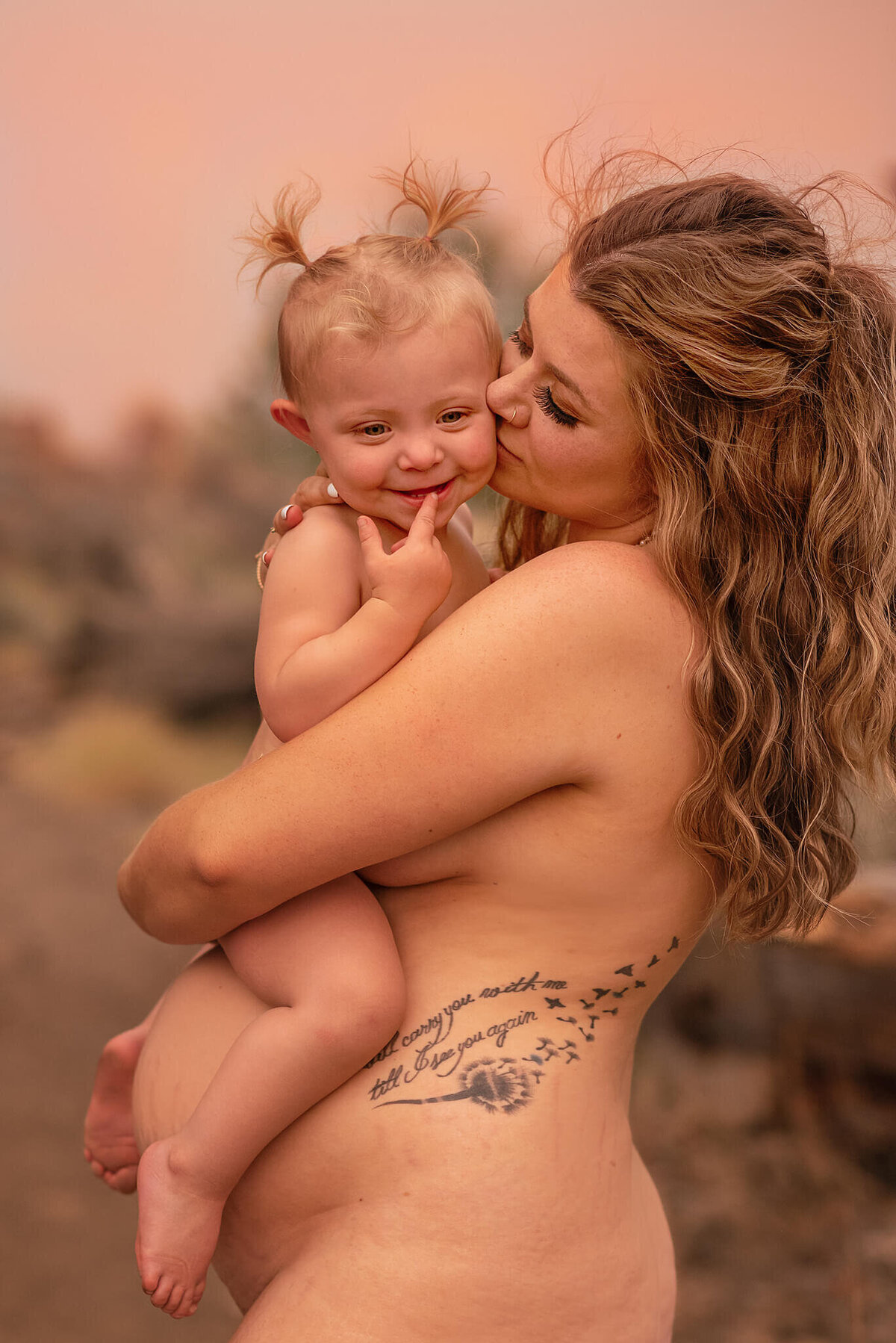 Image of a nude mother and daughter embracing on the moms pregnant belly. Captured by Brittany Danielle Photography in Kamloops BC