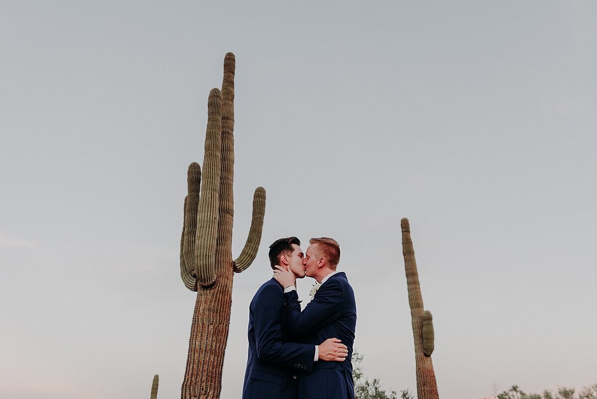 two grooms kiss under towering saguaro cactus