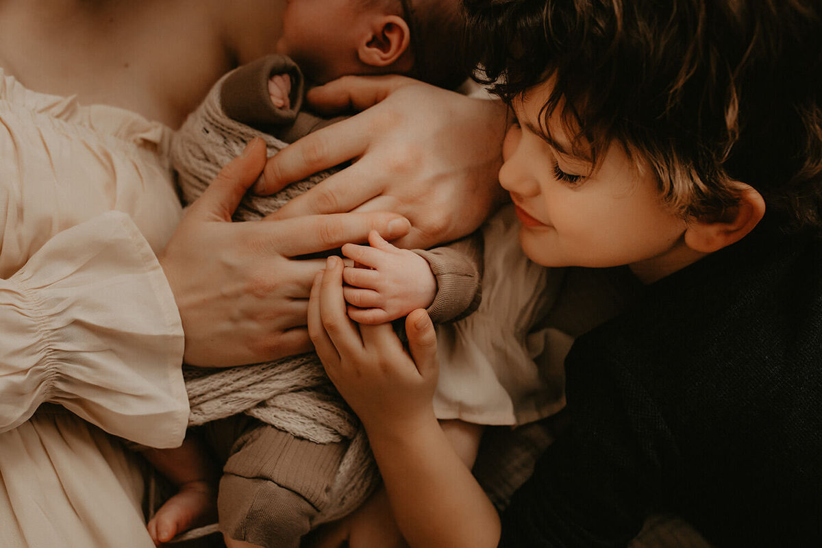 mom dad and brothers hands all laying on baby