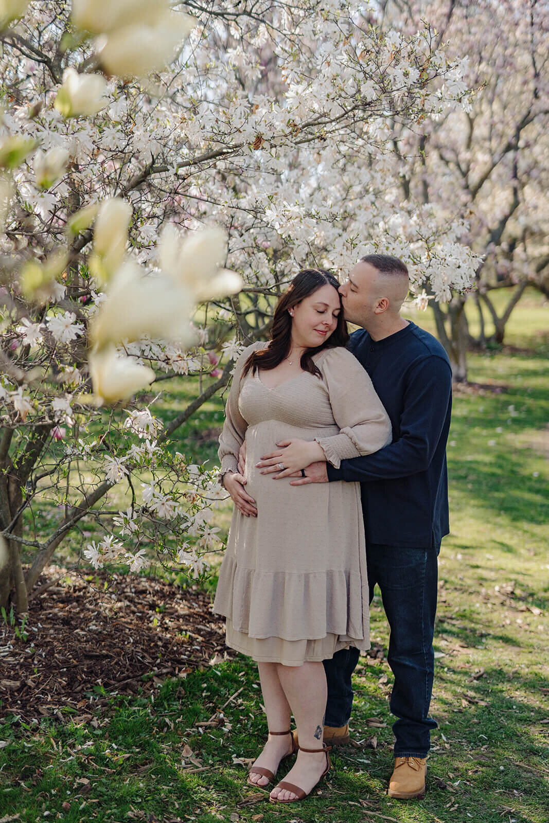 Couple with hands on baby bump standing by a tree in blossom at  Finger Lakes Maternity session