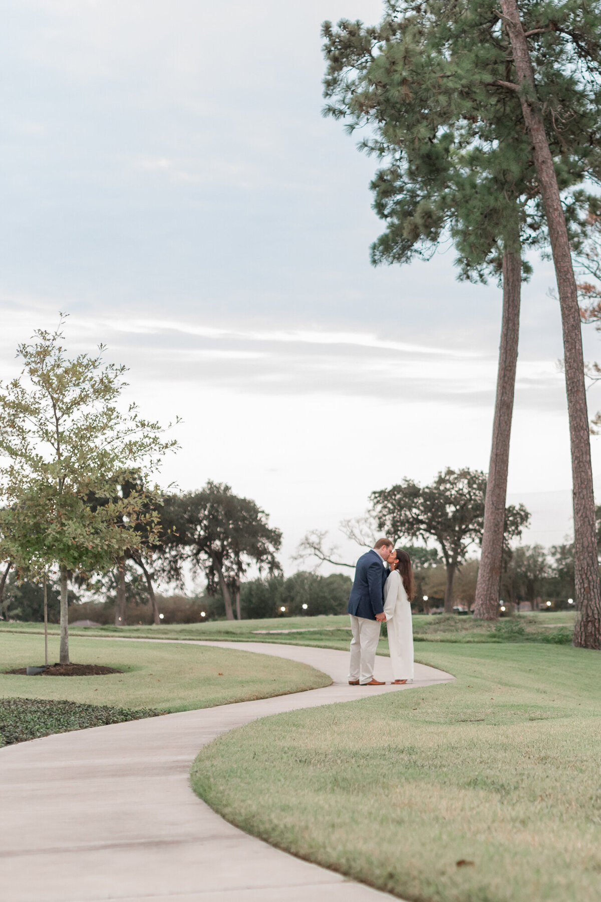 bride and groom kiss while standing alone a winding sidewalk at lakeside country club in houston,f or their rehearsal dinner