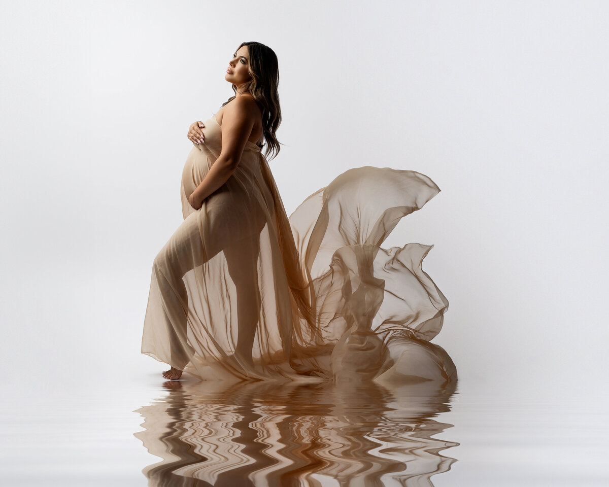 Beautiful expectant mother in a brown dress, posed in side view with a stunning water reflection on the ground, creating a serene and elegant atmosphere. Captured by Inland Empire maternity photographer Kaitlyn Dawn Photography.