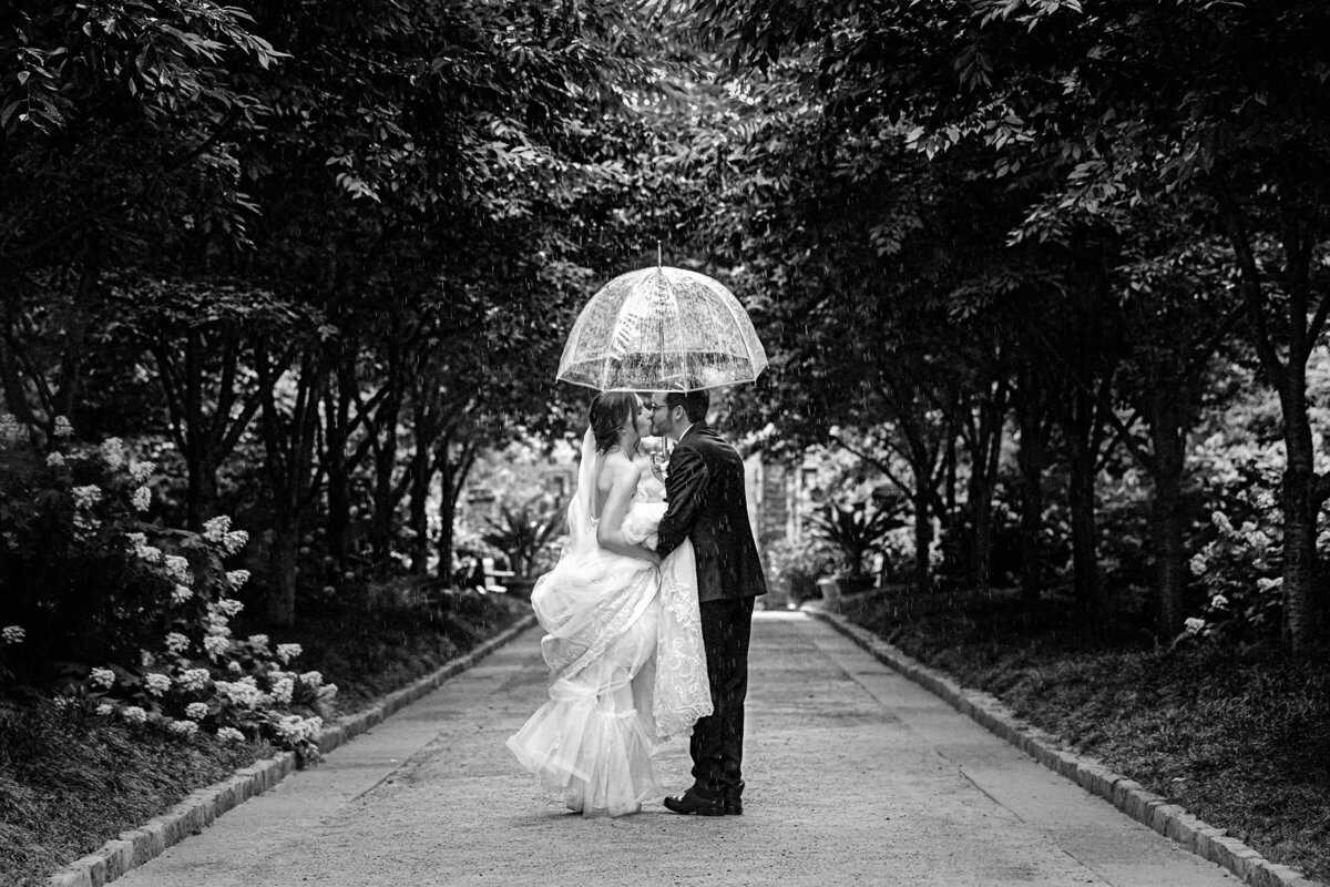 Bride and groom share a romantic moment under an umbrella on a rainy day,