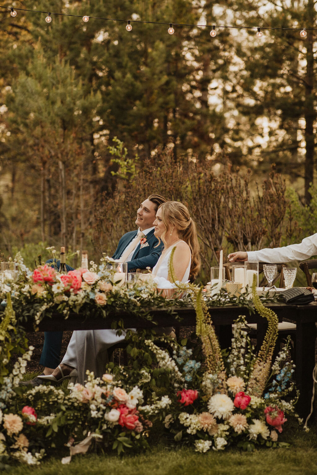 Bride and groom sitting at sweetheart table surrounded by flowers at private home in Sunriver