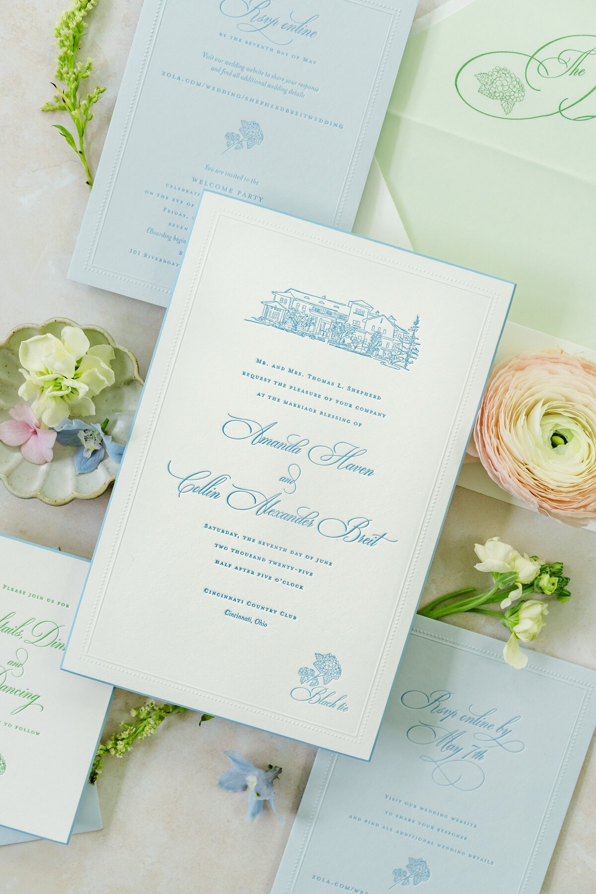 Wedding invitation suite with blue and green stationery surrounded by flowers.