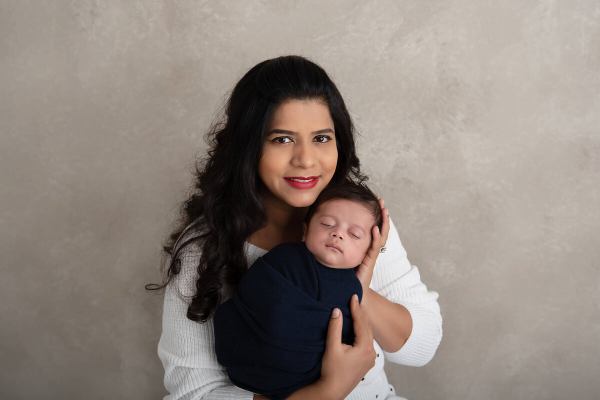 mom holding newborn baby boy wrapped in blue for his newborn photography session in Burlington, ON