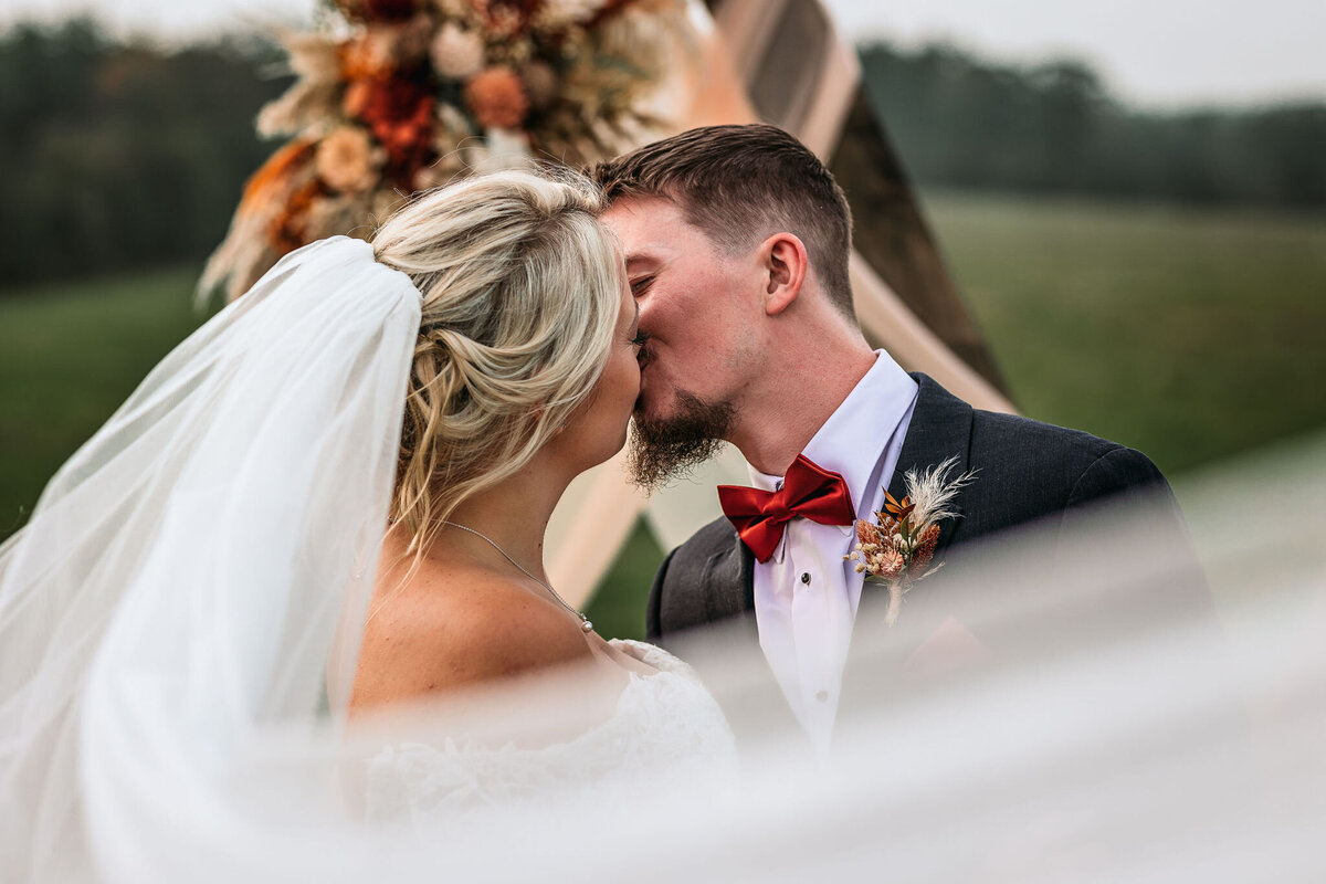 Bride and groom kissing as cathedral vail swoops across them at Sanborn Hil Farm wedding in Wakefield NH by Lisa Smith Photography